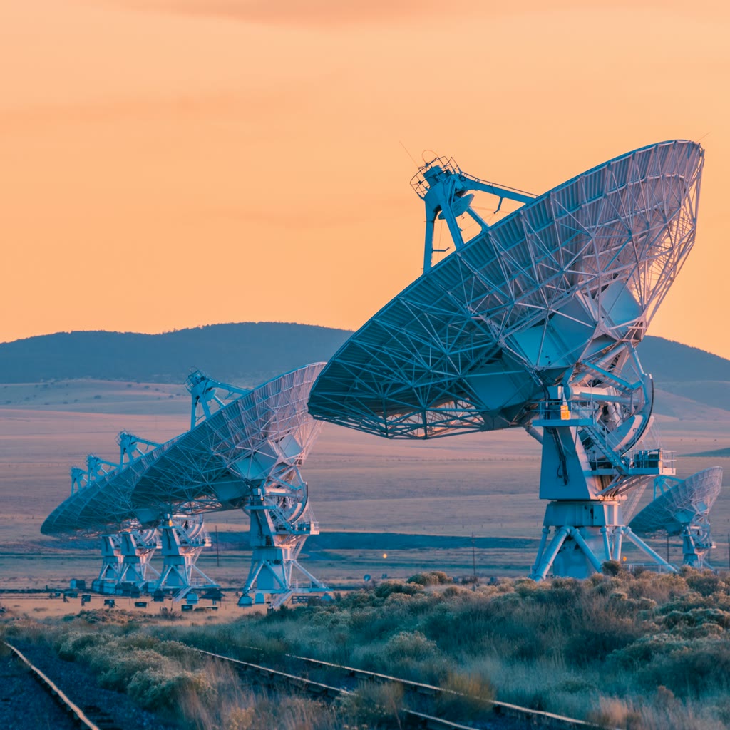 A group of radio telescope dishes beneath a warm, clouded sky.
